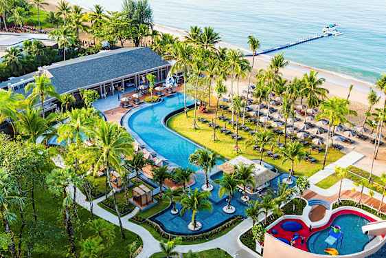 Ett tropiskt semesterområde med en stor pool, omgiven av palmer, solstolar och en barnpool. En sandstrand och havet syns i bakgrunden. (AI-genererad text)