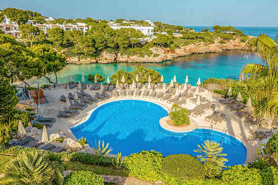 En utomhuspool med solstolar och parasoller, omgiven av grönska och med en utsikt över havet. (AI-genererad text)