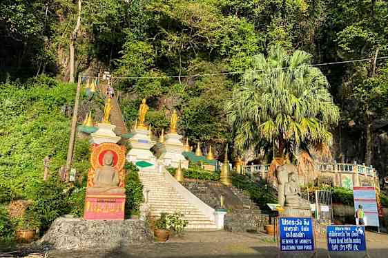 Bild av en trappa som leder upp till flera gyllene buddhistiska statyer och strukturer omgivna av grönska. (AI-genererad text)