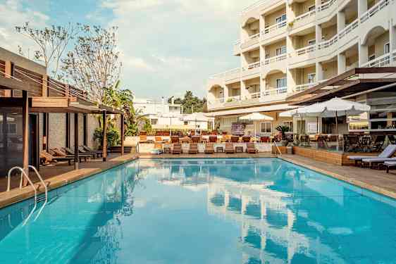 En utomhuspool med solstolar och parasoller vid sidan och ett fler våningshotell i bakgrunden. (AI-genererad text)