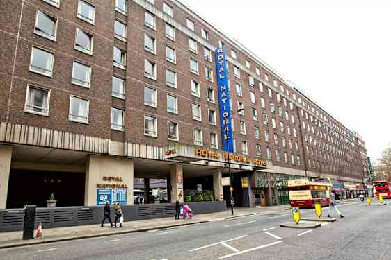 Bild av Royal National Hotel från gatan med flera bussar och gångtrafikanter. (AI-genererad text)