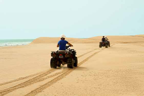 Två personer kör fyrhjulingar över en sandstrand med havet i bakgrunden. (AI-genererad text)