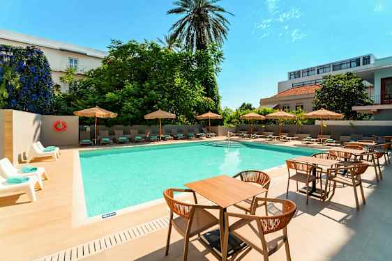 En utomhuspool med solstolar och parasoller vid sidan samt bord och stolar i förgrunden. (AI-genererad text)