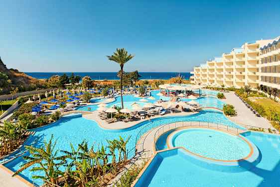 Bild av ett hotellområde med stora pooler och omgivande solstolar, samt havsutsikt i bakgrunden. (AI-genererad text)