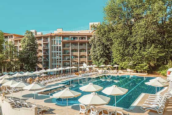 Poolområde med solstolar och parasoller, bakom syns en hotellbyggnad och gröna träd. (AI-genererad text)
