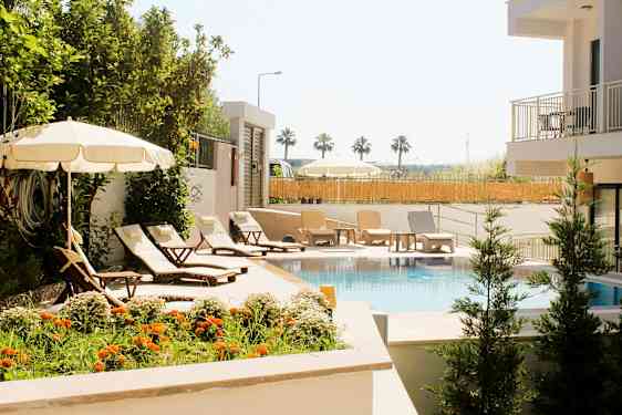 En pool omgiven av solstolar, parasoller och grönska. (AI-genererad text)