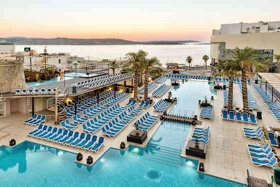 Stor poolområde med solstolar, palmer och utsikt över havet vid solnedgång. (AI-genererad text)