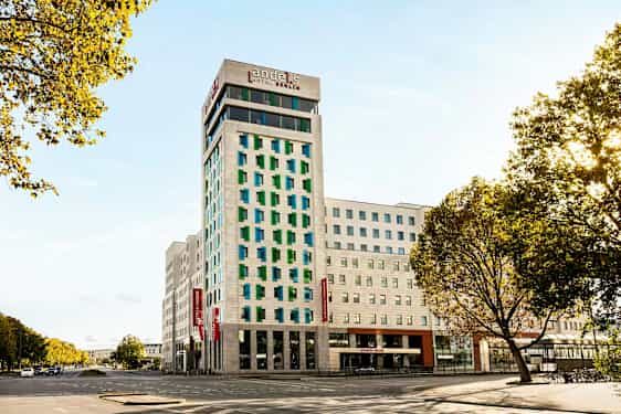 En modern hotellbyggnad med vit fasad och färgade fönster, omgiven av vägar och träd. (AI-genererad text)