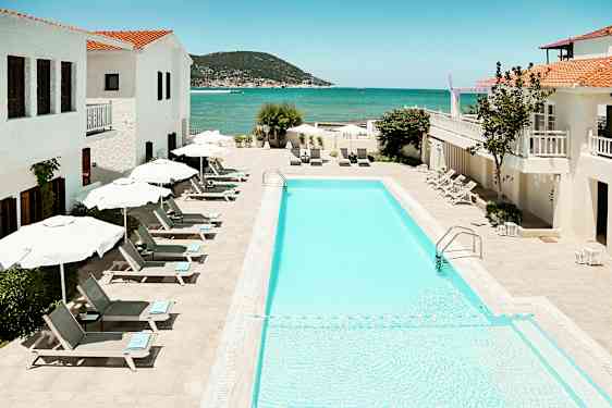 Bild av en utomhuspool med solstolar och parasoller, omgiven av vita byggnader med utsikt över havet. (AI-genererad text)