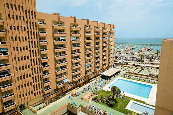 Ett höghus med balkonger och en pool framför samt en marina i bakgrunden. (AI-genererad text)