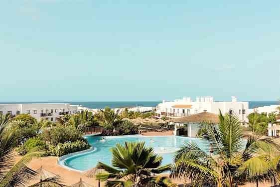 Hotellanläggning med pool, grönska och hav i bakgrunden. (AI-genererad text)