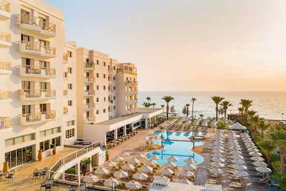 Hotell med balkonger, poolområde och hav i bakgrunden. (AI-genererad text)