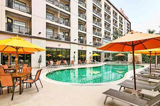 En hotellpool omgiven av solsängar och parasoller, med byggnaden i bakgrunden. (AI-genererad text)