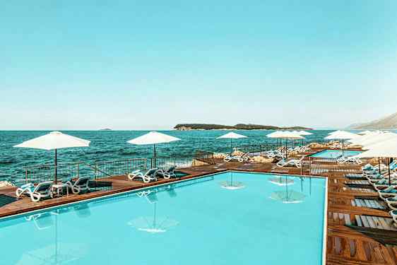 En swimmingpool vid havet, omgivet av solstolar och parasoller. (AI-genererad text)