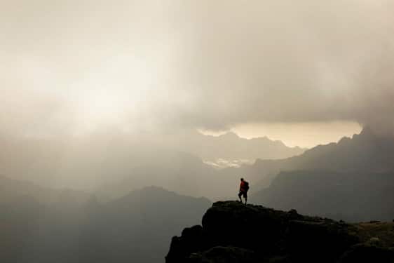 En vandringsman står på en bergstopp med dimmiga dalar och berg i bakgrunden. (AI-genererad text)