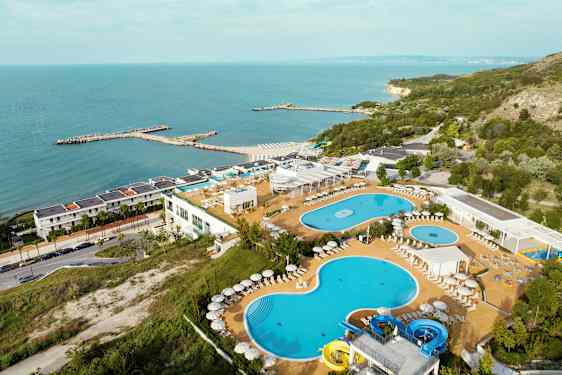 Bild av en resort vid havet med pooler, solstolar och en grönskande omgivning. (AI-genererad text)