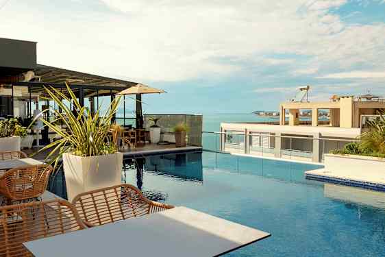 En takterrass med utsikt över havet, möblerad med bord, stolar och parasoller vid en swimmingpool. (AI-genererad text)