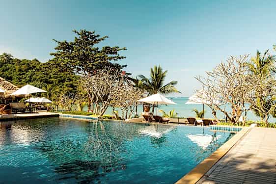 En infinitypool vid en strand med solstolar och parasoller i bakgrunden. (AI-genererad text)