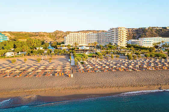 Strand med solparasoller och solstolar, hotell och grönska i bakgrunden. (AI-genererad text)