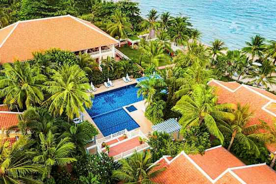 En tropisk resort med röda tak och en pool omgiven av palmer nära havet. (AI-genererad text)