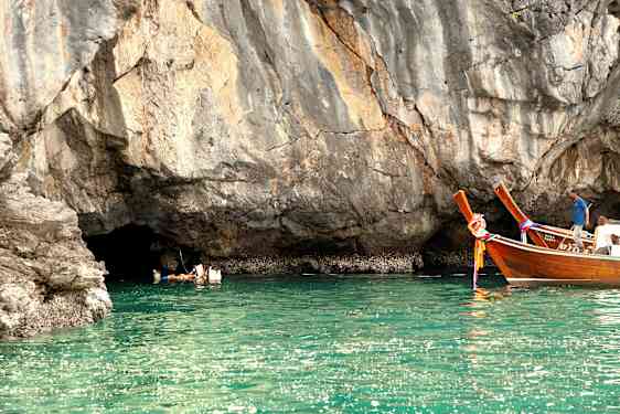 Personer simmar i vattnet vid en klippa, och två träfartyg flyter nära. (AI-genererad text)