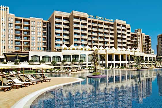 Ett hotell med flera våningar vid en stor poolomgiven av solstolar och parasoller. (AI-genererad text)