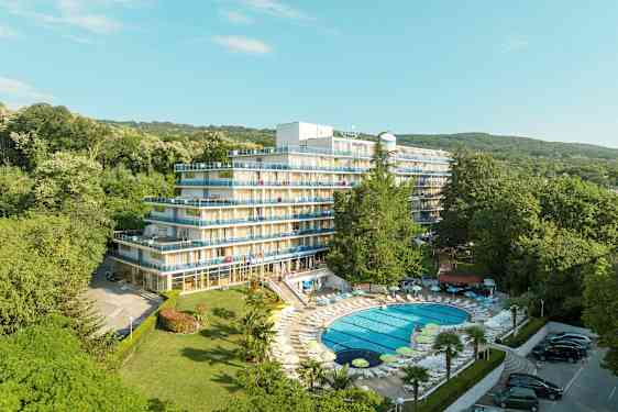 Bild av ett hotell med flera våningar och balkonger, omgiven av frodig grönska. En pool med solstolar ligger i förgrunden. (AI-genererad text)