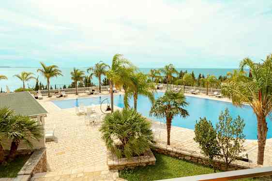 En utomhuspool med omgivande solstolar och palmer med utsikt över havet. (AI-genererad text)