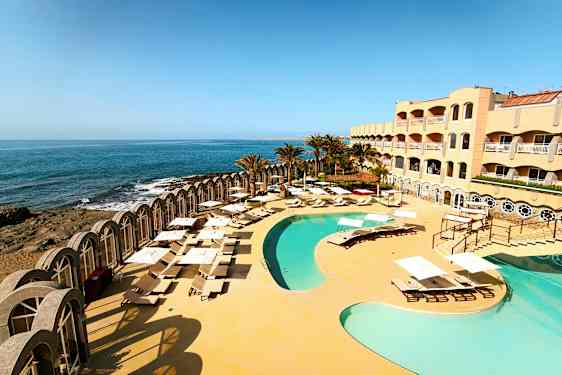Bild av ett hotellkomplex med pool och solstolar vid havet. (AI-genererad text)