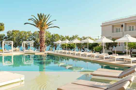 En pool med solstolar och parasoller vid ett hotell med havsutsikt. (AI-genererad text)