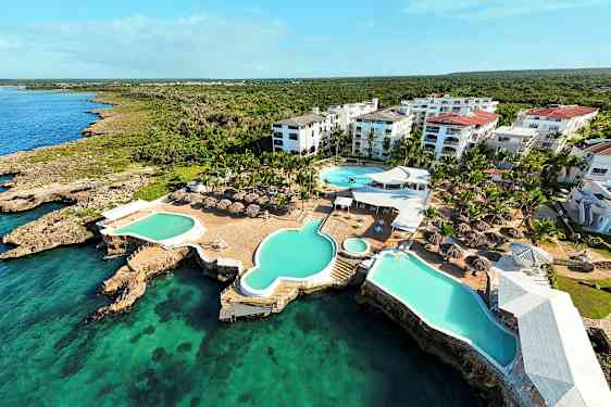 Flygbild över ett semesteranläggning med pooler och takparasoller vid havet. (AI-genererad text)