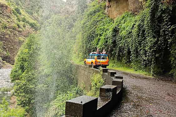 En gul-orange jeep på en väg vid ett vattenfall i en grön dal. (AI-genererad text)
