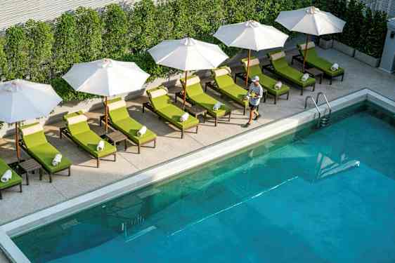 Pool med solstolar och parasoller vid kanten, samt en person som går förbi. (AI-genererad text)