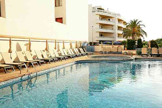 En utomhuspool omgiven av solstolar och parasoller, med en byggnad och en palm i bakgrunden. (AI-genererad text)