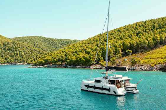 Segelbåt som ligger förtöjd vid en kust med grönskande kullar. (AI-genererad text)