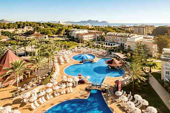 Hotellets poolområde med solstolar, parasoller och omgivande byggnader, med havet i bakgrunden. (AI-genererad text)