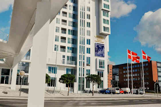 Modern byggnad med glasfasad intill en gata. Flaggan från Danmark syns på flaggstänger. (AI-genererad text)