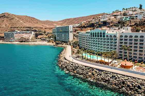 Hotell vid en kust med klippor, pool och palmer. (AI-genererad text)