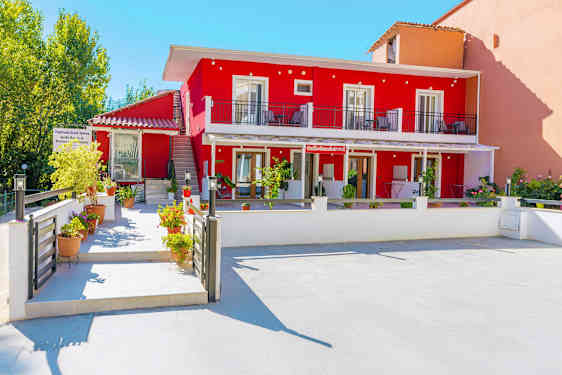 Bild som visar ett rött byggnad med balkonger och blomkrukor i förgrunden. (AI-genererad text)