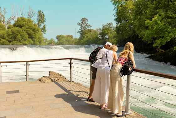 Tre personer lutar sig mot ett räcke och blickar ut över ett vattenfall. (AI-genererad text)
