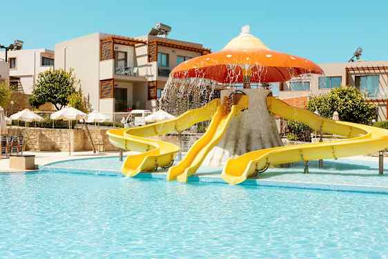 Vattenrutschbanor formade som en svamp vid en utomhuspool; bakomliggande byggnader och parasoller syns. (AI-genererad text)