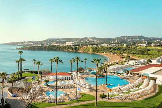 Utsikt över hotellområde med pooler och utsikt mot en vik med blått vatten och grönska i bakgrunden. (AI-genererad text)