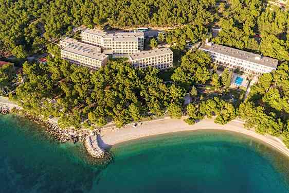 Flygbild över hotellkomplex omgivet av skog och strand. (AI-genererad text)