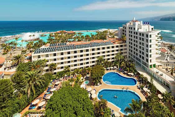 Hotellanläggning med pooler och grönska nära havet. (AI-genererad text)