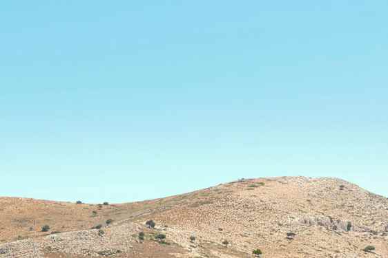 Bild av en klarblå havsvik med en sandstrand som har hus och kullar i bakgrunden. (AI-genererad text)