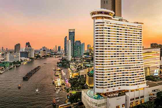 Vy över en flod som omges av höghus under en solnedgång. Ett stort hotell är synligt i förgrunden. (AI-genererad text)