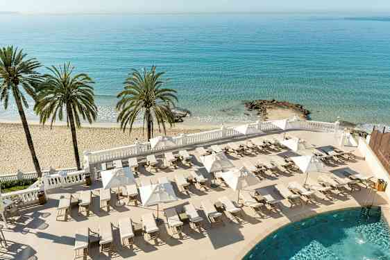 En strand med palmer, solstolar och parasoller vid ett blått hav. (AI-genererad text)