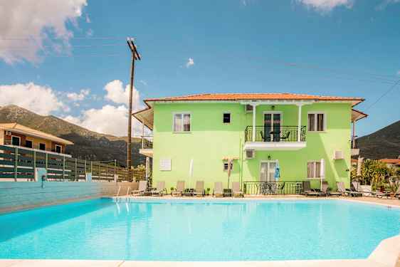 En ljusgrön byggnad med balkonger och solstolar, framför en utomhuspool. (AI-genererad text)