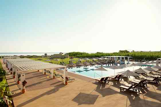 En utomhuspool med solstolar och parasoller på ett hotellområde vid havet. (AI-genererad text)