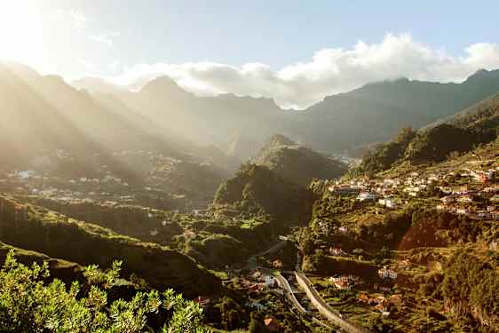 Vy över en grön dal med hus och berg i bakgrunden under en solig dag. (AI-genererad text)